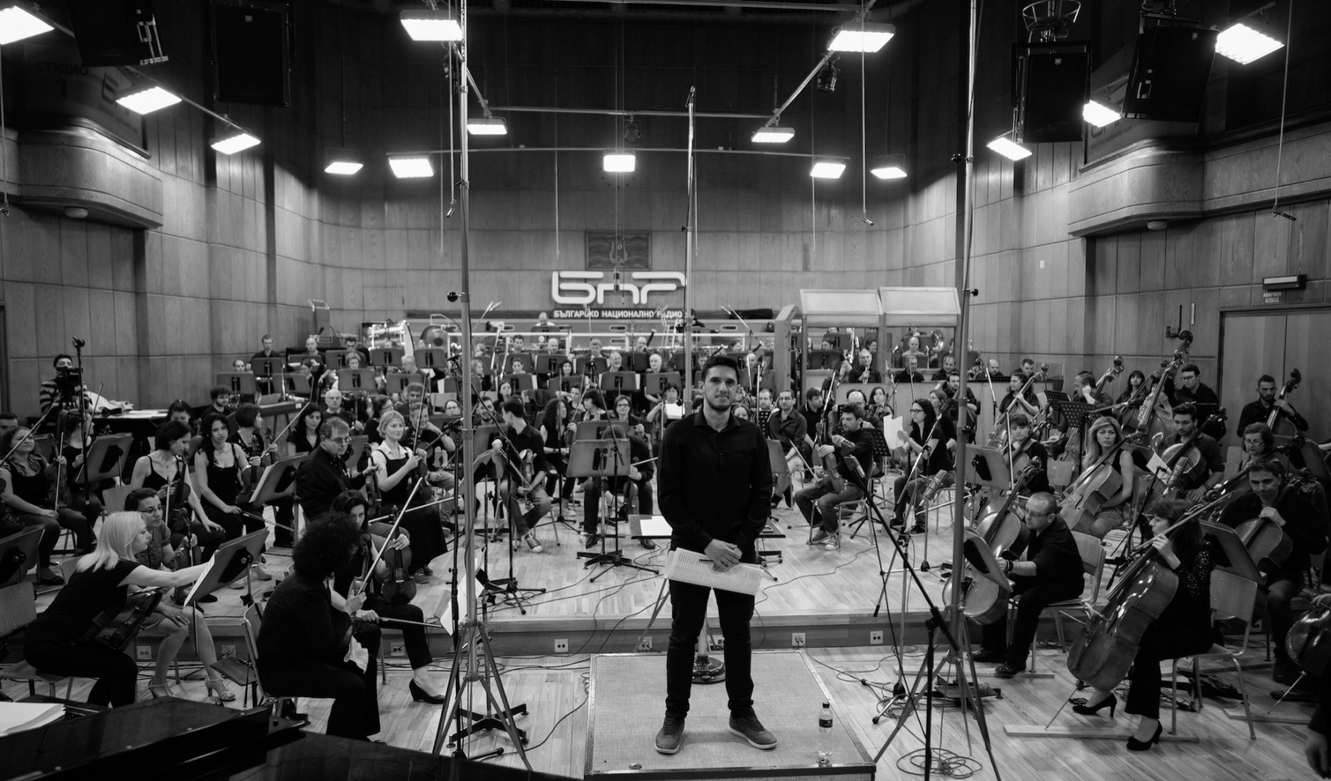 Edu Prado standing in front of a full symphony orchestra at the Bulgarian National Radio studio